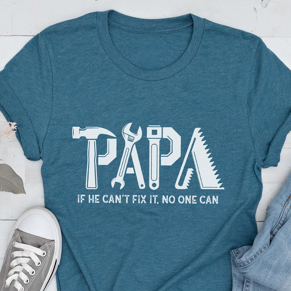 May include: Teal t-shirt with the word "PAPA" in white, using tool-themed letters. Below, the text reads "IF HE CAN'T FIX IT, NO ONE CAN". A hammer, wrench, saw, and other tools form the letters.
