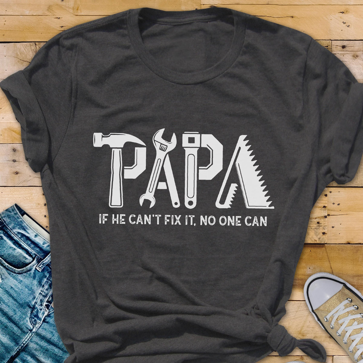 May include: Dark gray t-shirt with the word "PAPA" in white, each letter designed as a tool: hammer, wrench, screwdriver, and saw. The text "IF HE CAN'T FIX IT, NO ONE CAN" is below the word "PAPA".