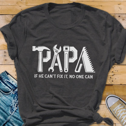 May include: Dark gray t-shirt with the word "PAPA" in white, each letter designed as a tool: hammer, wrench, screwdriver, and saw. The text "IF HE CAN'T FIX IT, NO ONE CAN" is below the word "PAPA".