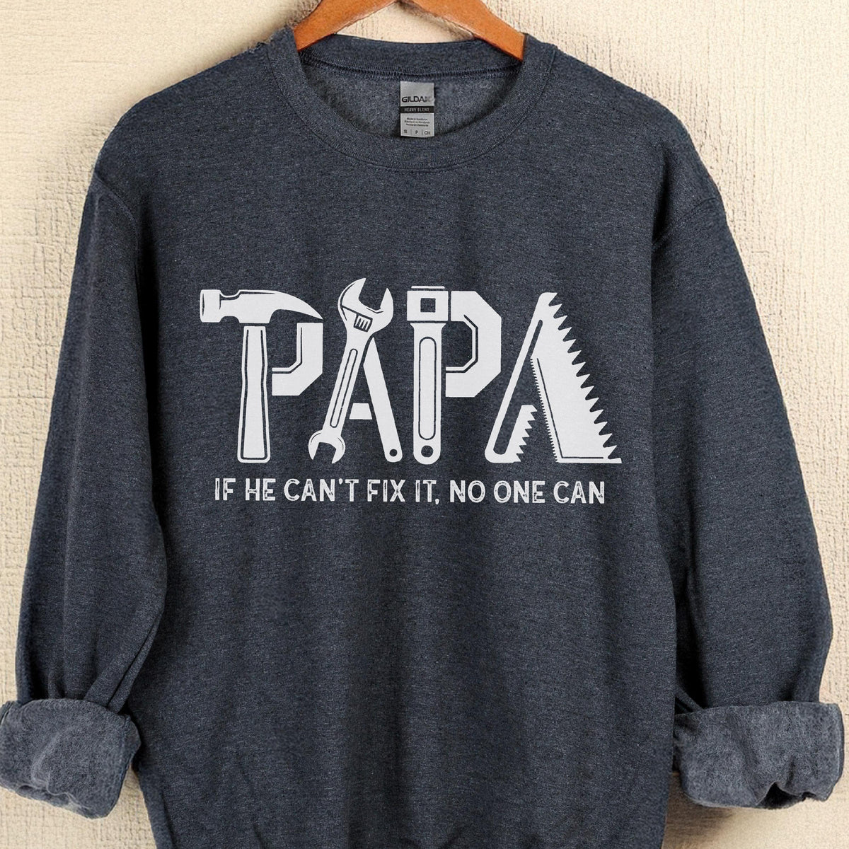 May include: A navy blue sweatshirt with the word "PAPA" in white, with each letter designed as a tool: a hammer, wrench, adjustable wrench, and saw. The text "IF HE CAN'T FIX IT, NO ONE CAN" is below the word "PAPA".