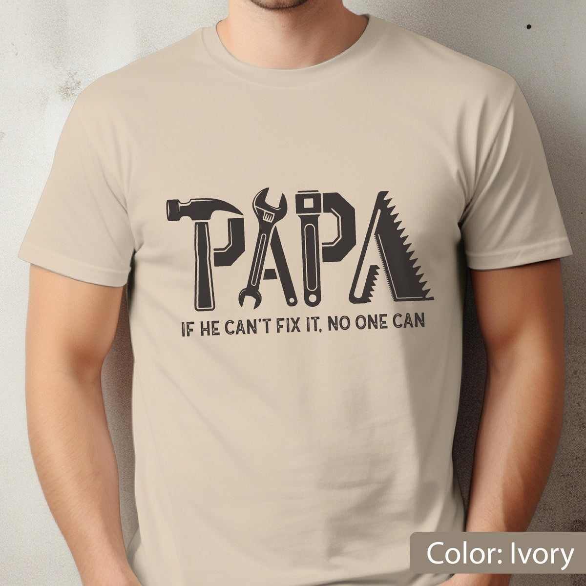 May include: Ivory-colored t-shirt with the word "PAPA" formed by tools: a hammer, wrench, and saw. The text "IF HE CAN'T FIX IT, NO ONE CAN" is below the word "PAPA".