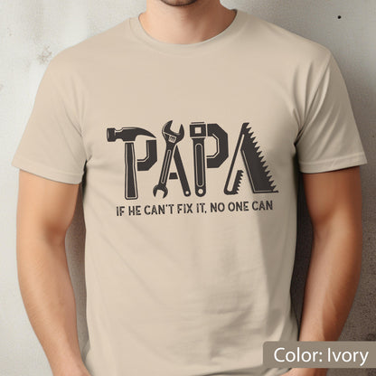 May include: Ivory-colored t-shirt with the word "PAPA" formed by tools: a hammer, wrench, and saw. The text "IF HE CAN'T FIX IT, NO ONE CAN" is below the word "PAPA".