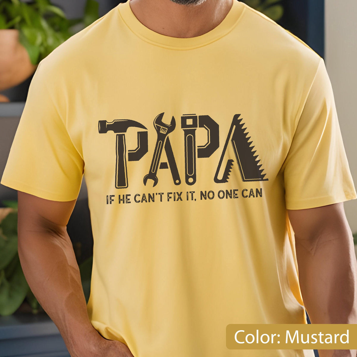 May include: Mustard yellow t-shirt with a black graphic that spells "PAPA" using tools like a hammer, wrench, and saw. The text below reads "IF HE CAN'T FIX IT, NO ONE CAN."