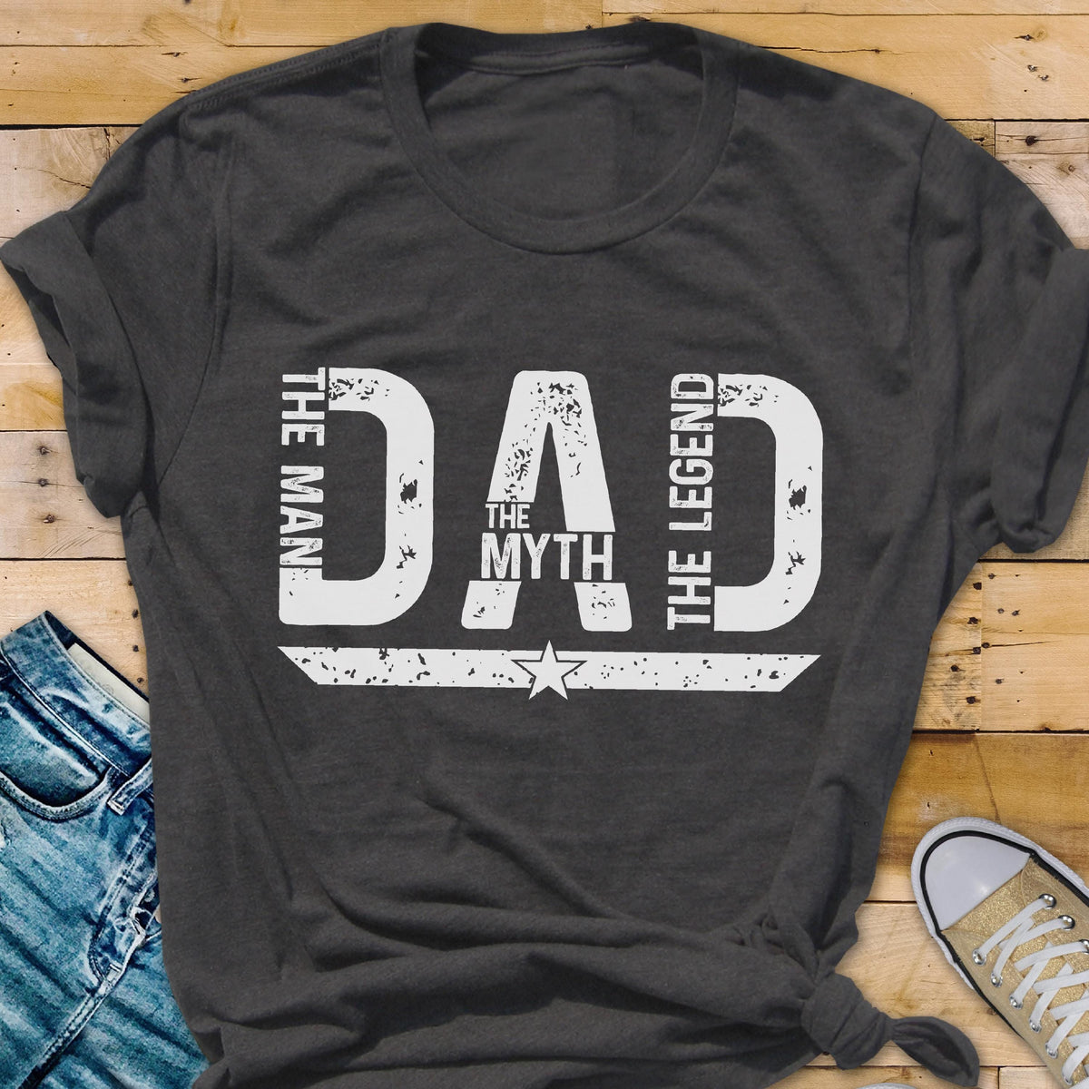 May include: Dark gray t-shirt with the word "DAD" in large white letters. The words "THE MAN", "THE MYTH", and "THE LEGEND" are also printed on the shirt in white. A white star is below the word "MYTH".
