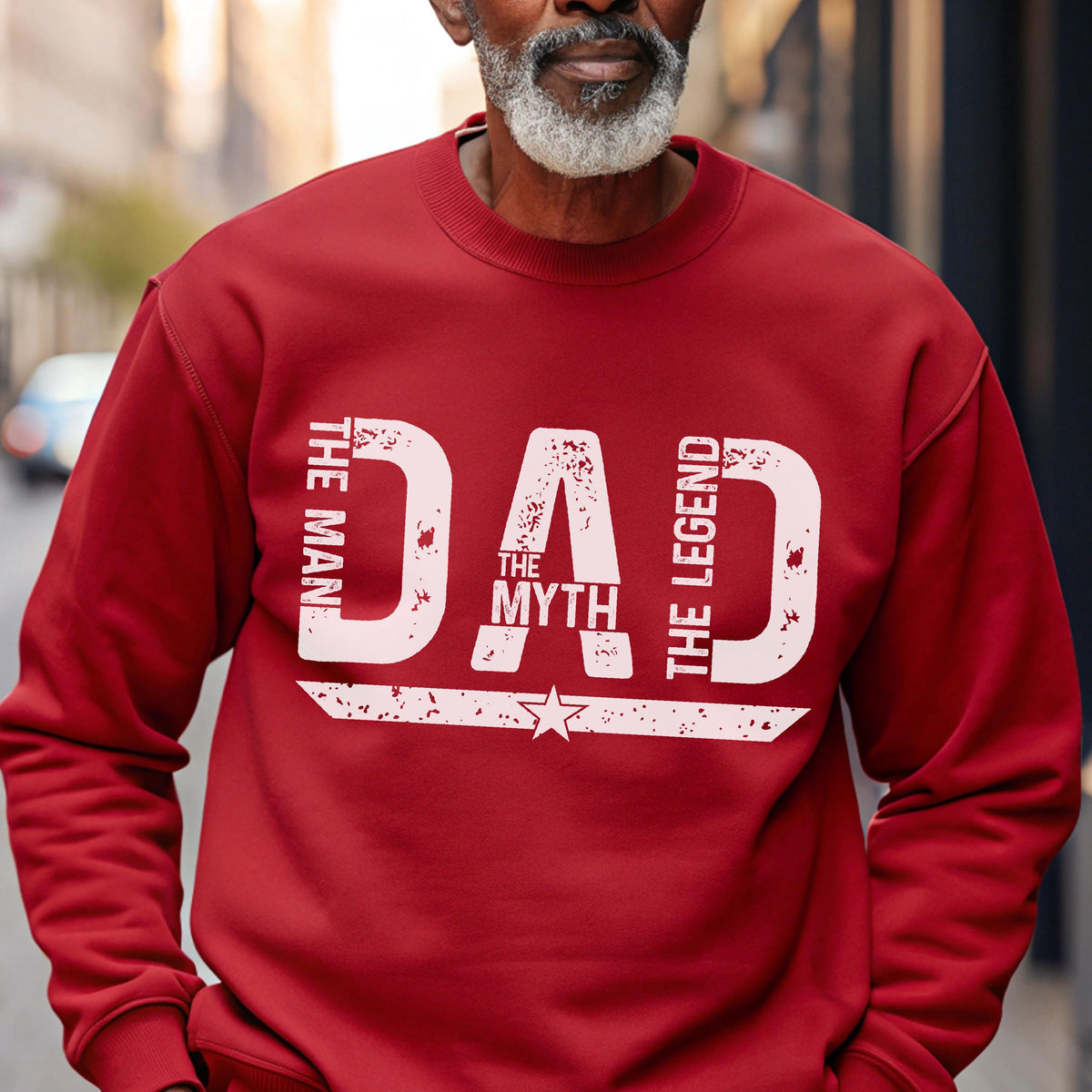 May include: A red sweatshirt with the words "DAD THE MYTH THE LEGEND" printed in white. The text is arranged vertically and horizontally, with a star graphic below the word "MYTH". The sweatshirt is a solid color and has a crew neck.