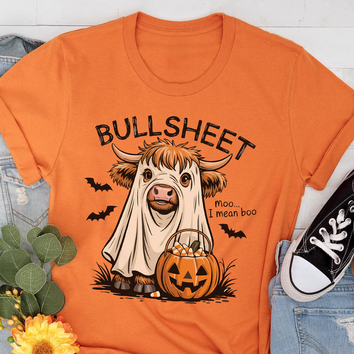 May include: Orange t-shirt with a Halloween-themed graphic. The design features a cow dressed as a ghost, a jack-o'-lantern, and the text "BULLSHEET" above and "Moo... I mean boo" below. Black bats are scattered around the cow.