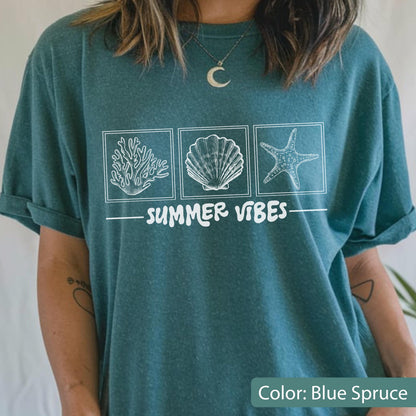 May include: Blue spruce t-shirt with a white graphic of coral, a seashell, and a starfish in square frames. The words "SUMMER VIBES" are printed below the images. The shirt has rolled-up sleeves.