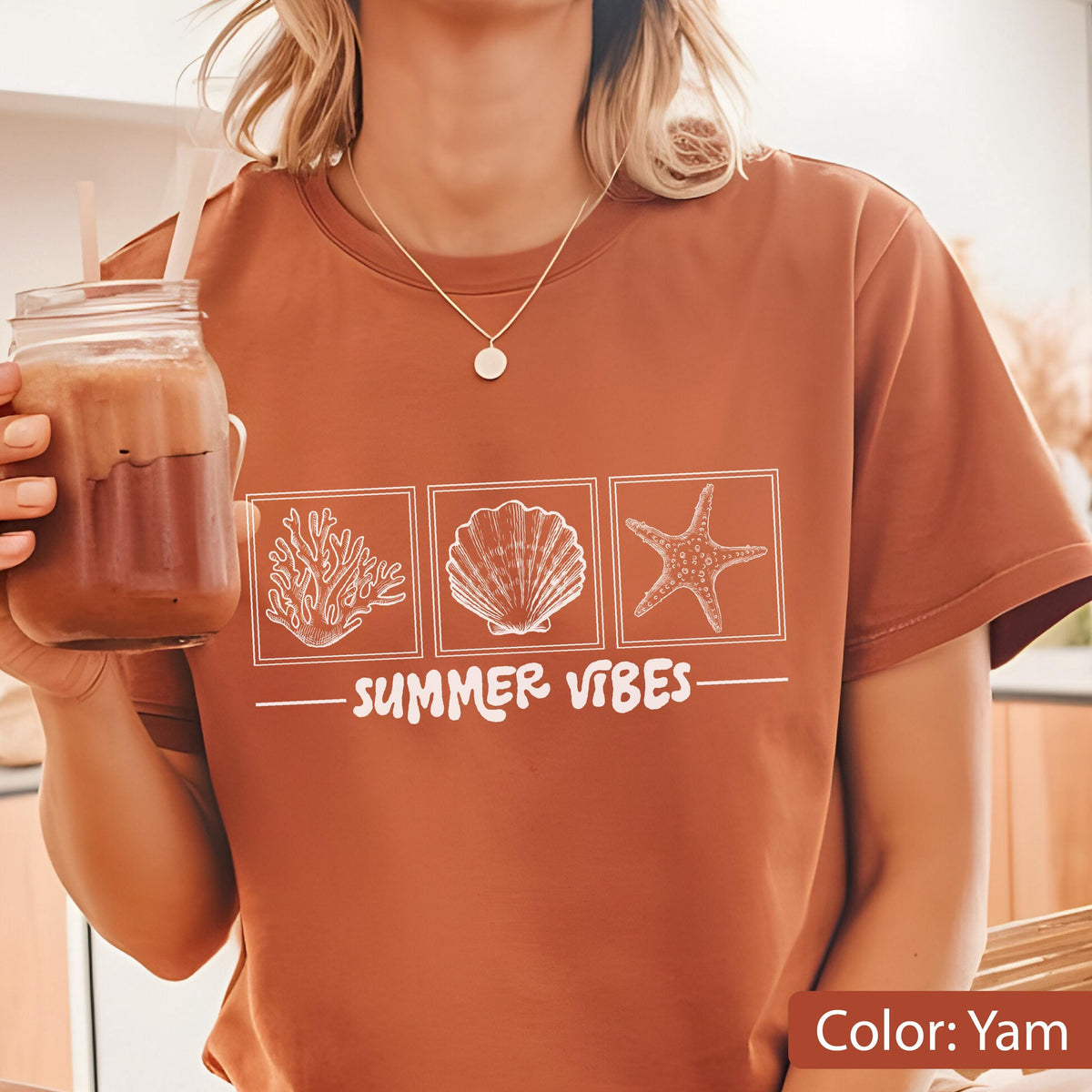 May include: Yam-colored t-shirt with a white graphic of coral, a seashell, and a starfish, with the words "SUMMER VIBES" underneath. The shirt has short sleeves and a round neckline.