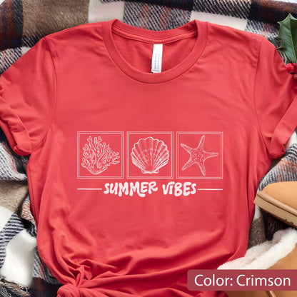 May include: Crimson red t-shirt with a white graphic of coral, a seashell, and a starfish. The text "SUMMER VIBES" is printed below the images. The shirt is made of a soft material.