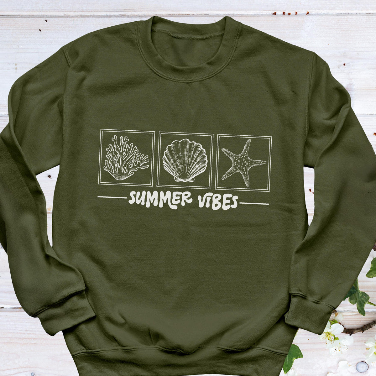 May include: Olive green sweatshirt with a white graphic of coral, a seashell, and a starfish in square frames. Below the images is the text "SUMMER VIBES" in white. The sweatshirt is a casual, long-sleeved garment.