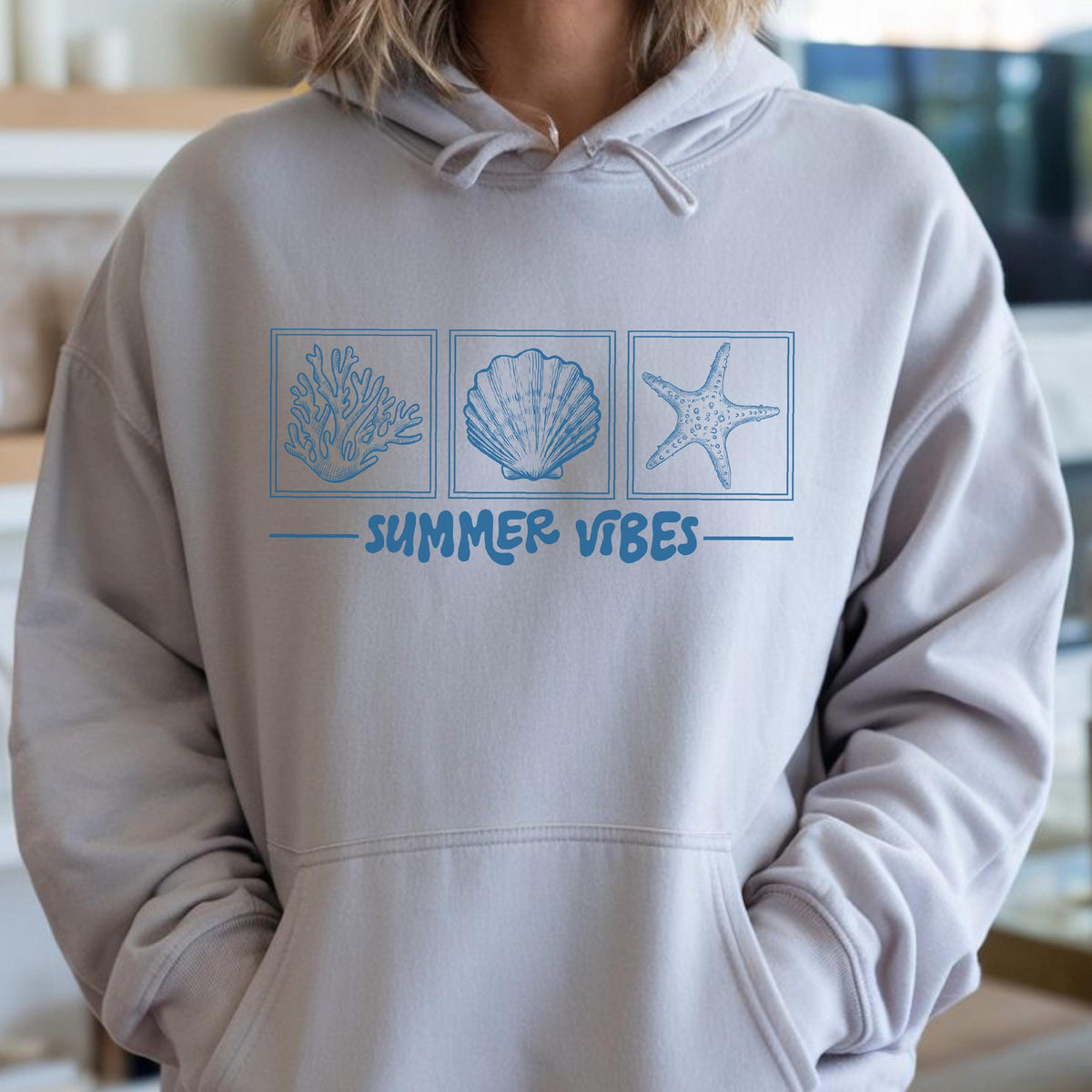 May include: A light gray hoodie with a front pocket and drawstring hood. The front features three blue square illustrations of coral, a seashell, and a starfish, with the words "SUMMER VIBES" below.
