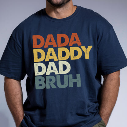 May include: Navy blue t-shirt with the words "DADA DADDY DAD BRUH" in orange, yellow, off-white, and green. The text is stacked vertically, creating a retro, vintage look. A casual, comfortable tee.