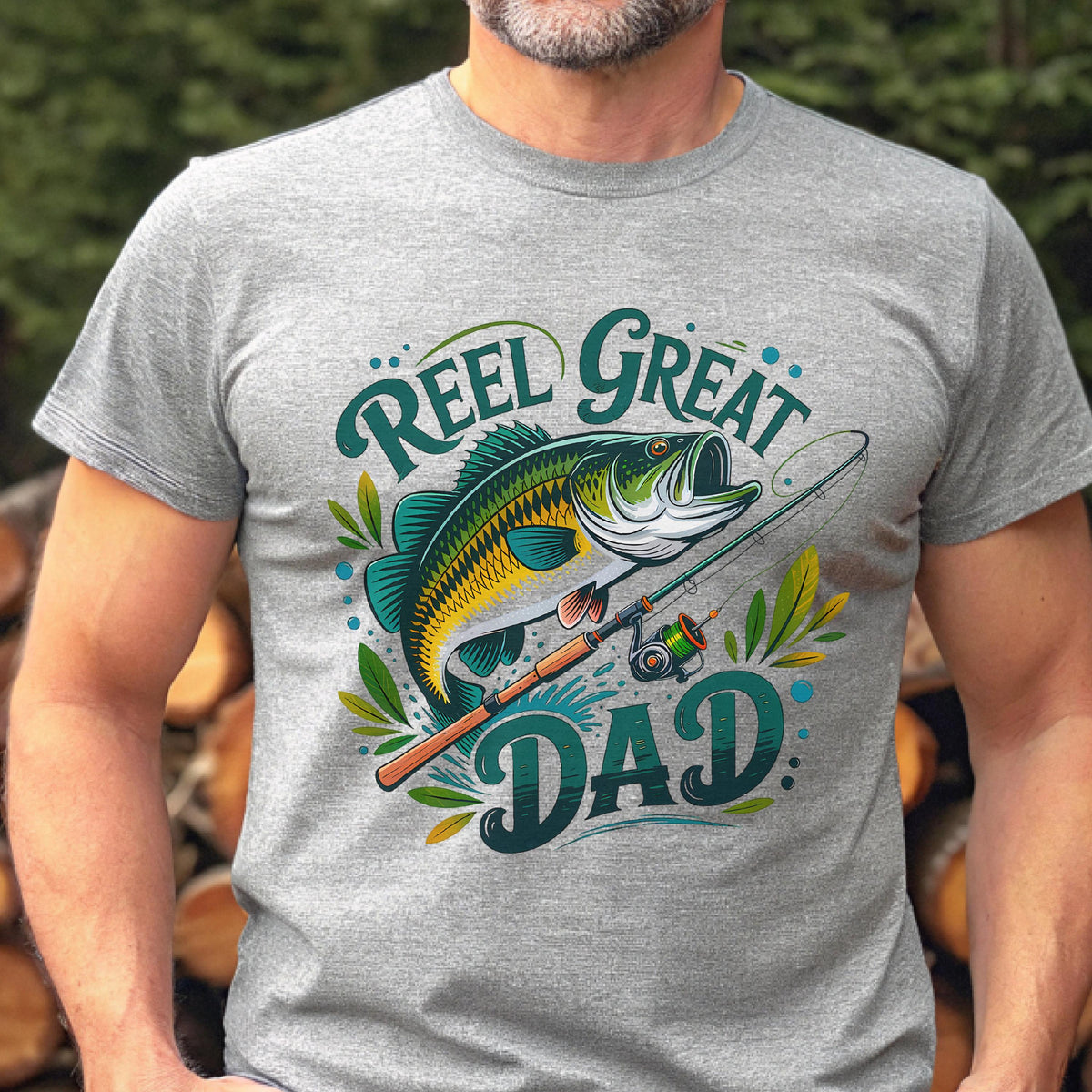 May include: Gray t-shirt with a colorful graphic of a largemouth bass, fishing rod, and the words "Reel Great Dad" in teal. The fish is green, yellow, and white. The shirt is short-sleeved and made of a soft material.