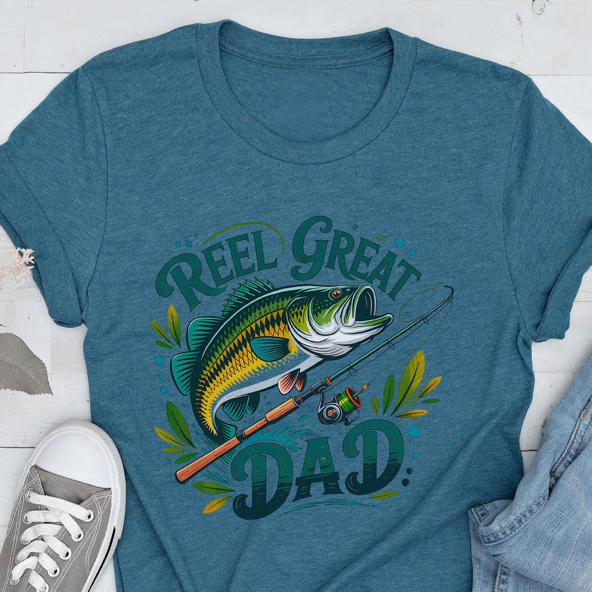 May include: Teal t-shirt with a graphic of a fish, fishing rod, and the words "Reel Great Dad." The fish is green, yellow, and black. The text is in green. The fishing rod is brown and the reel is green.