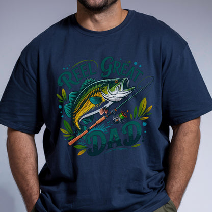 May include: Navy blue t-shirt with a colorful graphic of a fish, fishing rod, and the words "Reel Great Dad." The design features shades of green, yellow, and white. A perfect gift for fishing enthusiasts.