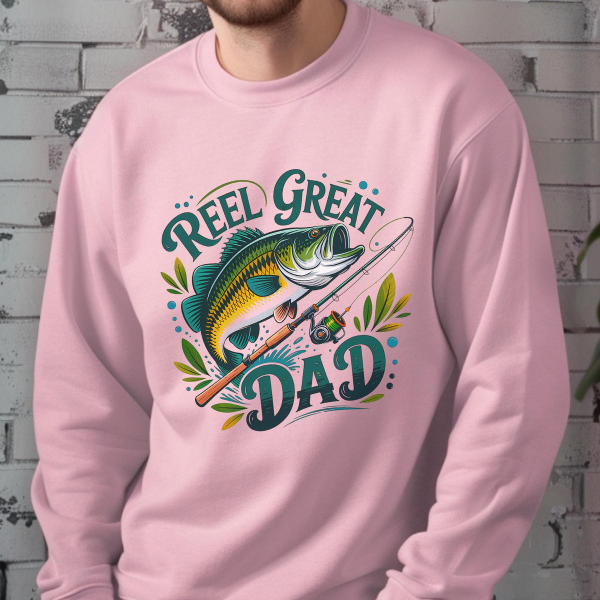 May include: Pink sweatshirt with a graphic of a fish, fishing rod, and the words "Reel Great Dad" in teal and yellow. The fish is green, yellow, and black. The sweatshirt is a solid light pink color.