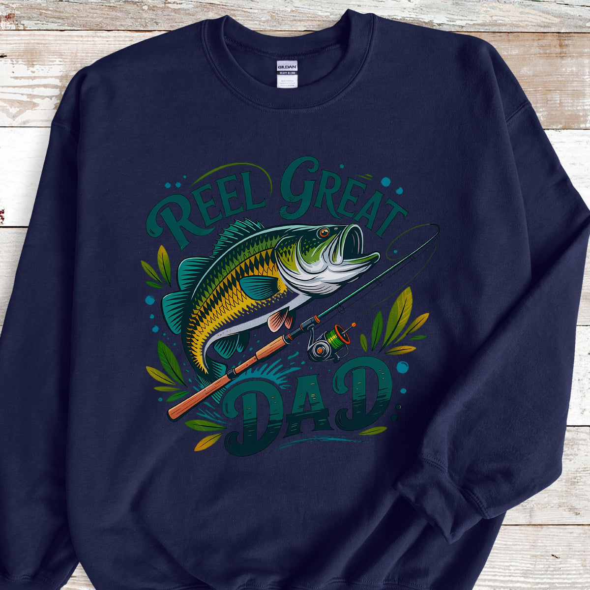 May include: Navy blue sweatshirt with a graphic of a largemouth bass and fishing rod. Text reads "Reel Great Dad" in green and teal. The fish is yellow, green, and blue. A great gift for a fishing enthusiast.