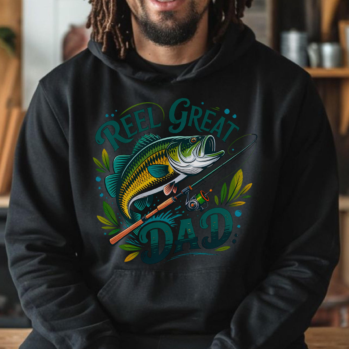 May include: Black hoodie with a colorful graphic of a fish, fishing rod, and the words "Reel Great Dad" in teal and green. The design features a detailed illustration of a largemouth bass and fishing gear.