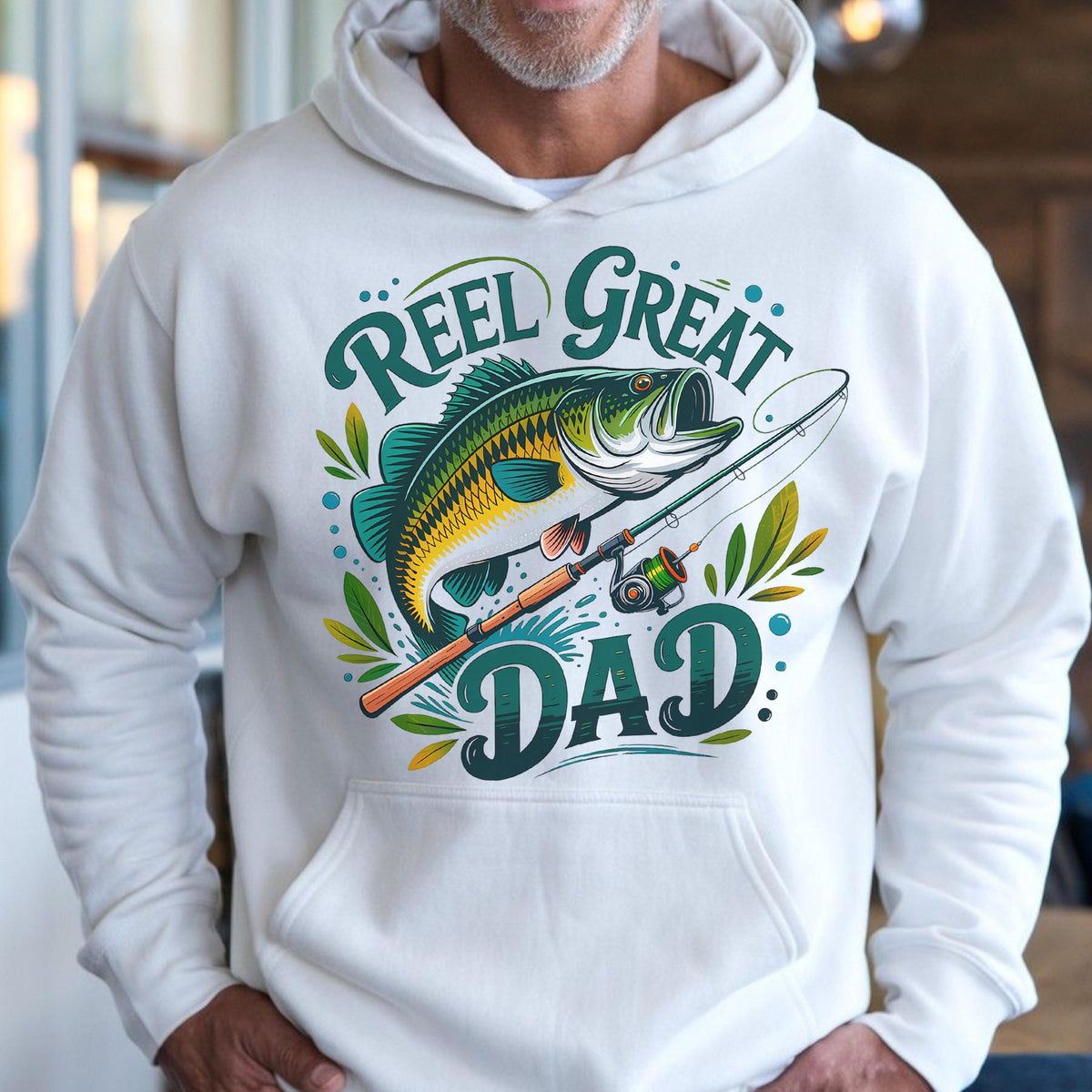May include: White hoodie with a fishing-themed graphic. The design features a green and yellow fish, a fishing rod, and the words "Reel Great Dad" in green and teal. The hoodie has a drawstring hood and a front pocket.