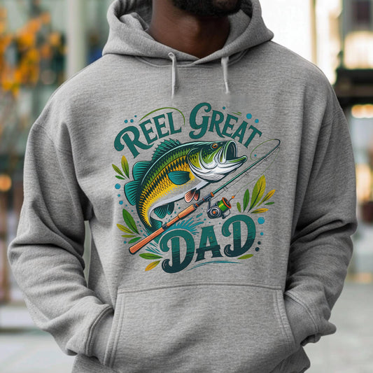 May include: A gray hoodie featuring a graphic of a fish, fishing rod, and the words "Reel Great Dad" in teal and white. The design includes leaves and dots, creating a fishing-themed design.