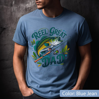 May include: Blue jean-colored t-shirt featuring a graphic of a largemouth bass with a fishing rod and the words "Reel Great Dad" in a stylized font. The design includes green and yellow accents, suggesting a fishing theme.