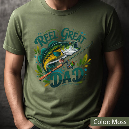 May include: Moss green t-shirt featuring a graphic of a fish, fishing rod, and the words "Reel Great Dad" in teal and yellow. The fish is green, yellow, and black. The shirt is a short-sleeved crew neck.