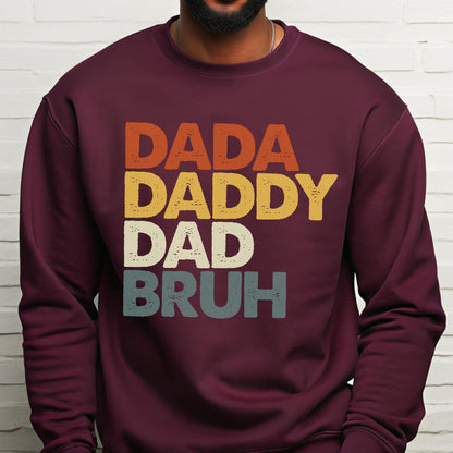 May include: Burgundy sweatshirt with the words "DADA DADDY DAD BRUH" in orange, yellow, white, and blue-green block letters. The sweatshirt has a crew neck and long sleeves.