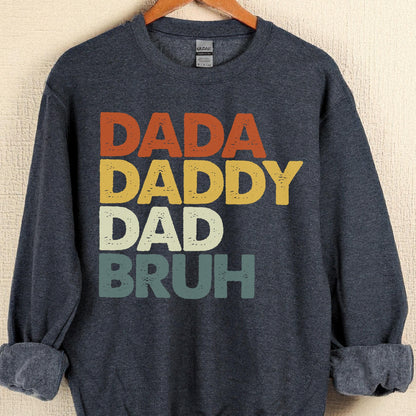 May include: A navy blue sweatshirt with the words "DADA DADDY DAD BRUH" in orange, yellow, white, and teal lettering. The sweatshirt has long sleeves and a crew neck.