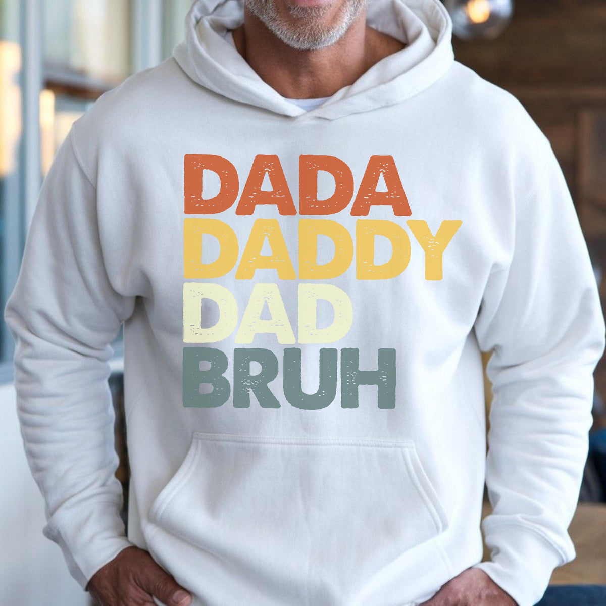 May include: A white hooded sweatshirt with the words "DADA DADDY DAD BRUH" printed in orange, yellow, light green, and teal. The sweatshirt has a front pocket and a drawstring hood.