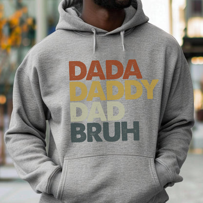 May include: A gray hoodie with the words "DADA DADDY DAD BRUH" printed in a retro style. The text is in shades of red, yellow, and green. The hoodie has a drawstring hood and a front pocket.