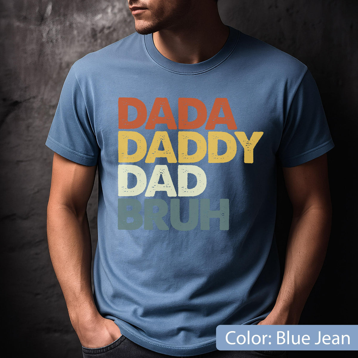 May include: Blue jean t-shirt with the words "DADA DADDY DAD BRUH" in orange, yellow, white, and green lettering. The shirt is a solid color and has a crew neck.