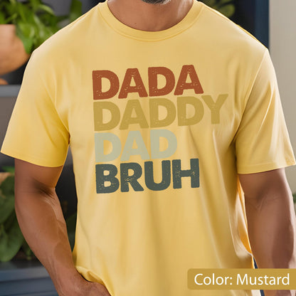 May include: Mustard yellow t-shirt with the words "DADA DADDY DAD BRUH" in a stacked design. The text is in shades of brown, yellow, and green. The shirt is short-sleeved.