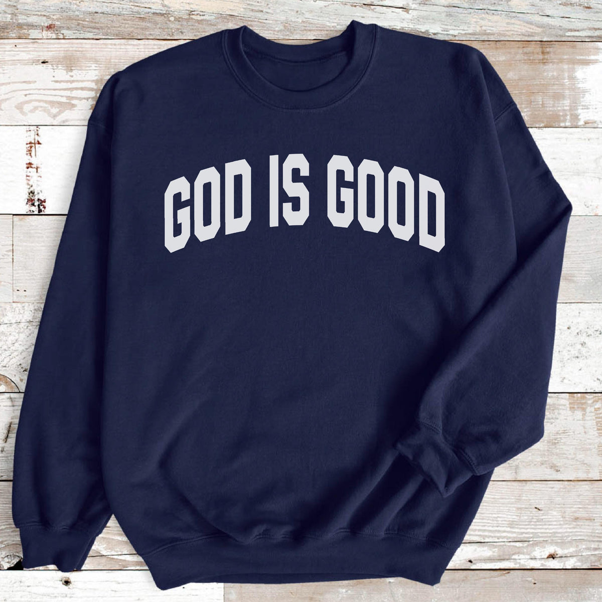 May include: Navy blue sweatshirt with the white text "GOD IS GOOD" in a bold, arched font. The crew neck sweatshirt has long sleeves and a relaxed fit, suitable for casual wear.