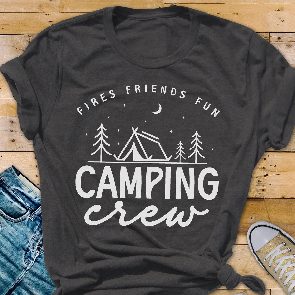 May include: Dark gray t-shirt with white text that reads "Fires Friends Fun" above a tent and trees graphic, with the words "Camping Crew" below. The shirt is folded and has a knot at the bottom.