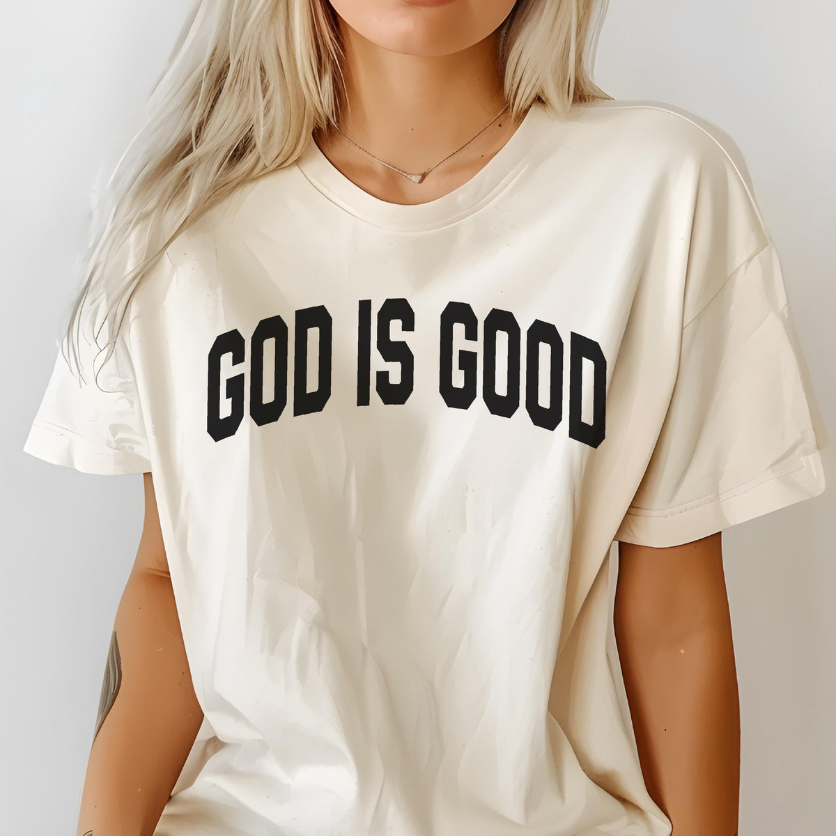May include: Cream-colored t-shirt with the text "GOD IS GOOD" in bold, black, block letters. The shirt has short sleeves and a crew neck. The overall style is casual and comfortable.