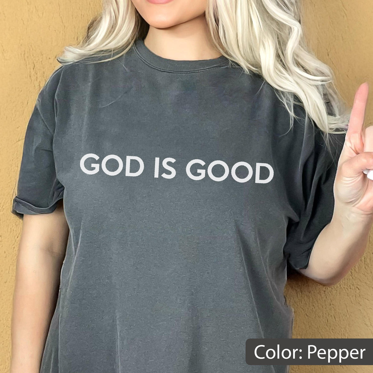 May include: Pepper-colored t-shirt with the text "GOD IS GOOD" in white. The shirt has a classic crew neck and short sleeves. The image shows a person wearing the shirt.