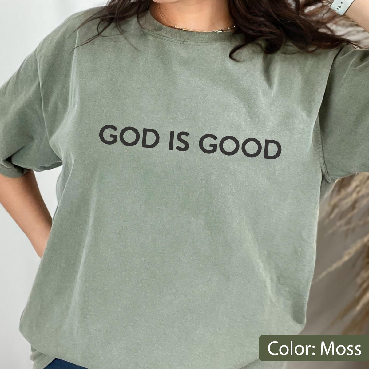 May include: Moss green t-shirt with the text "GOD IS GOOD" in black block letters. The shirt has a crew neck and short sleeves. The color is described as "Moss".