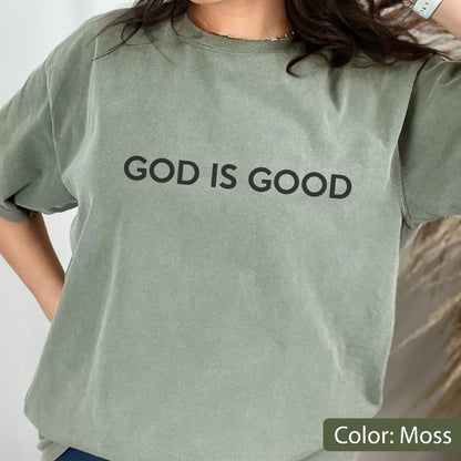 May include: Moss green t-shirt with the text "GOD IS GOOD" in black block letters. The shirt has a crew neck and short sleeves. The color is described as "Moss".