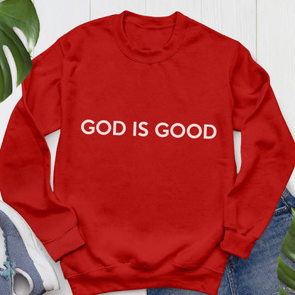 May include: A red sweatshirt with the white text "GOD IS GOOD" across the chest. The sweatshirt is a solid color and appears to be made of a soft material. The image is taken from a slightly elevated angle.