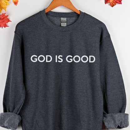 May include: Dark gray sweatshirt with the white text "GOD IS GOOD" across the chest. The sweatshirt has a crew neck and long sleeves with ribbed cuffs. The Gildan brand label is visible at the back of the neck.