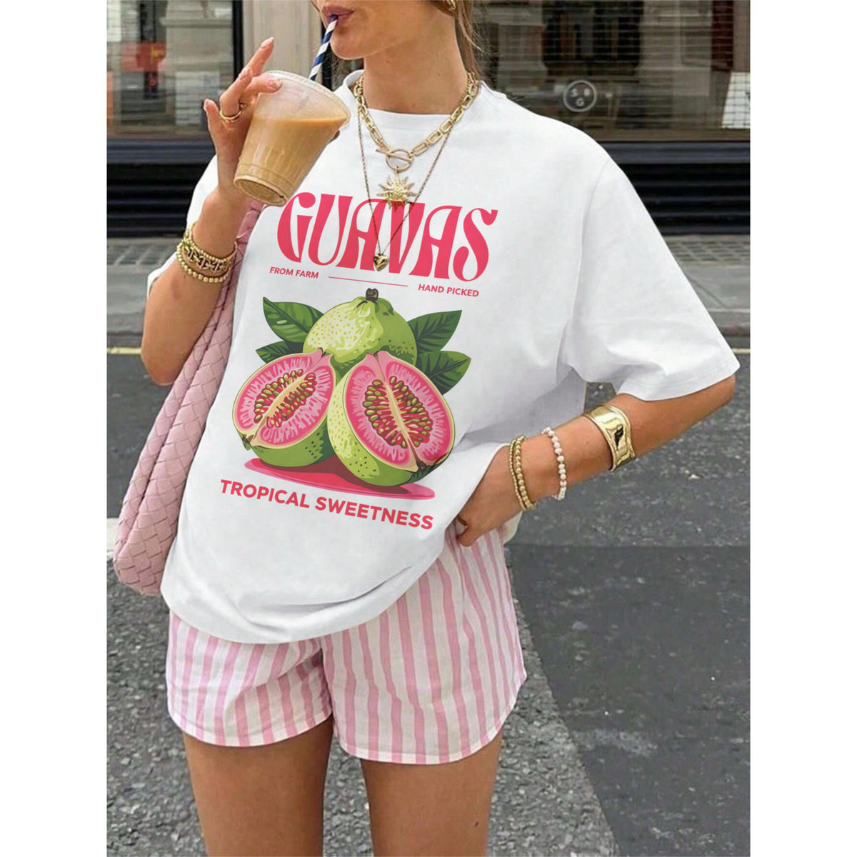 May include: White t-shirt with a guava fruit graphic and the text "GUAVAS" in red. The shirt also features the text "FROM FARM HAND PICKED TROPICAL SWEETNESS". The shirt is paired with pink and white striped shorts.