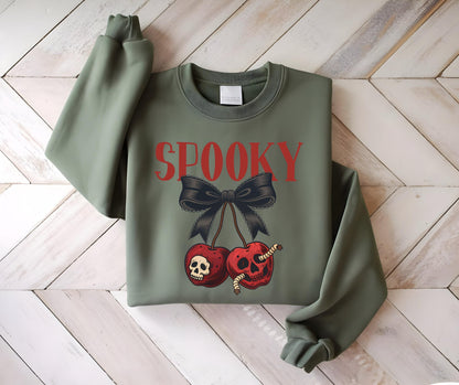 May include: An olive green sweatshirt with the word "SPOOKY" in red letters. Below the text is a black bow and two cherries with skull faces and worms. The sweatshirt has long sleeves and a crew neck.