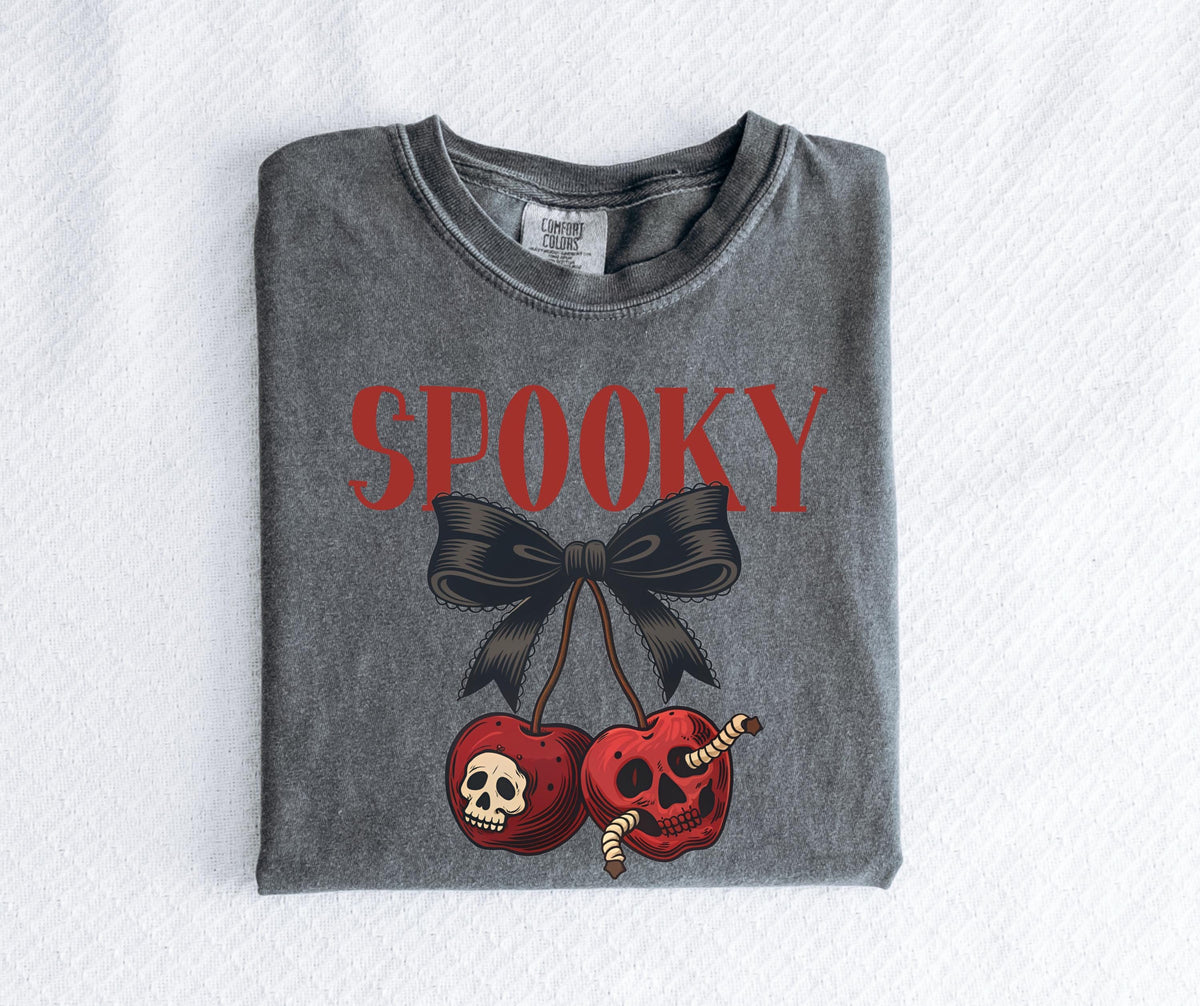 May include: A gray t-shirt with the word "SPOOKY" in red block letters above a black bow and two red cherries. The cherries have skull faces and worms. The shirt is folded on a white surface.