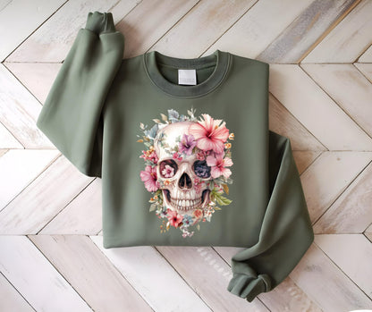 May include: Olive green sweatshirt featuring a floral skull design. The skull is adorned with pink, purple, and blue flowers. The sweatshirt has long sleeves and a crew neck. The design is centered on the front of the garment.