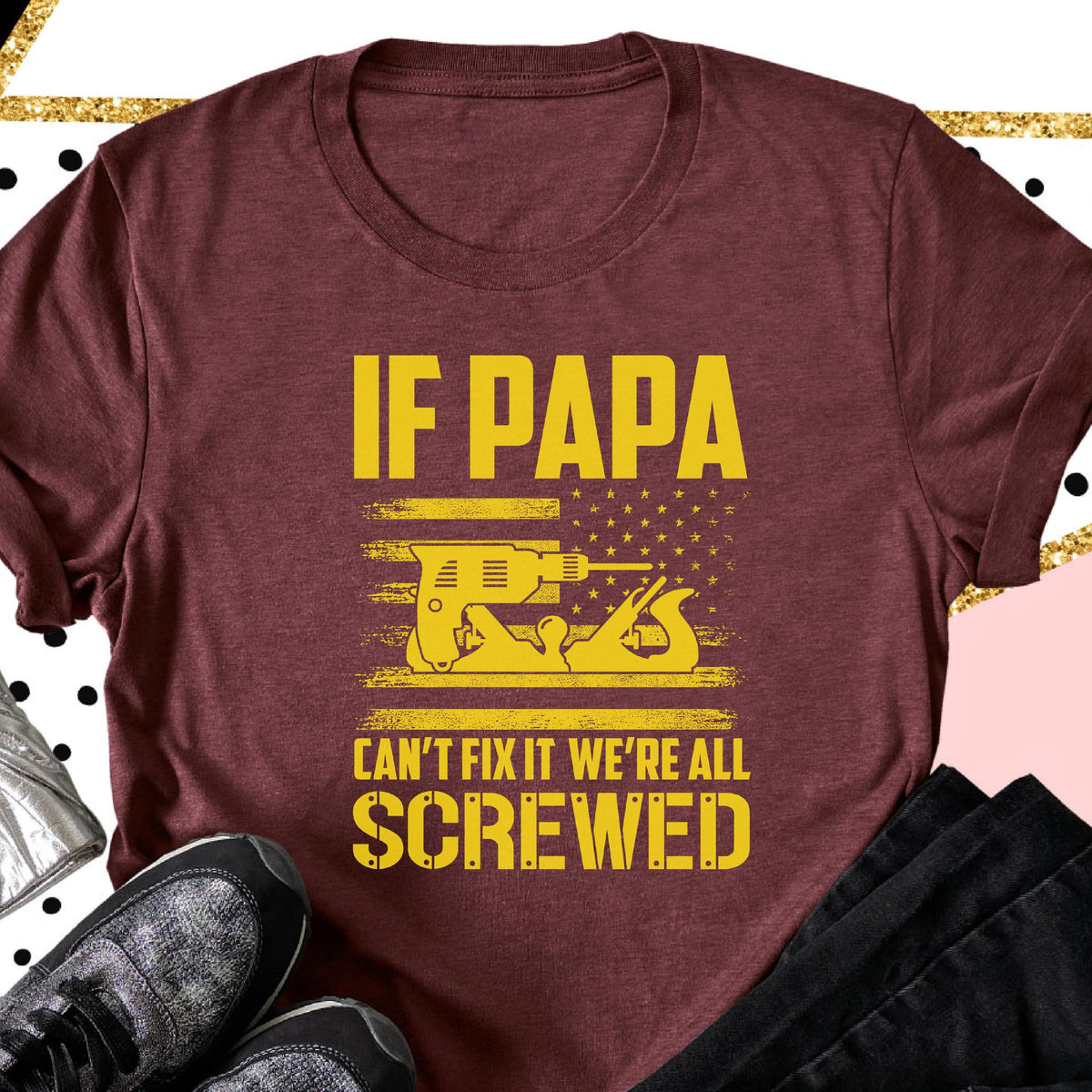 May include: Burgundy t-shirt with the text "IF PAPA CAN'T FIX IT WE'RE ALL SCREWED" in yellow. The design includes a yellow illustration of a drill and a hand plane, set against a stylized American flag.