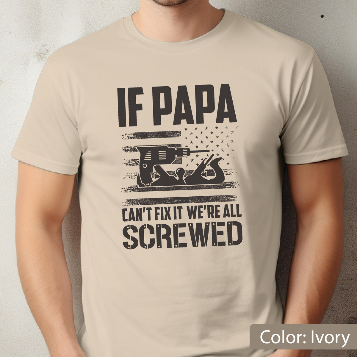 May include: Ivory-colored t-shirt with a graphic design. The design features the text "IF PAPA CAN'T FIX IT WE'RE ALL SCREWED" in black, along with an illustration of tools and an American flag.