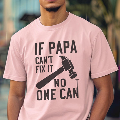 May include: A light pink t-shirt with the text "IF PAPA CAN'T FIX IT NO ONE CAN" in black. A hammer and nail graphic are featured below the text. The shirt is short-sleeved and made of a soft material.