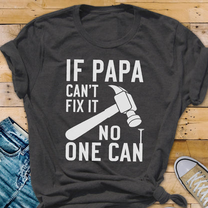 May include: Dark gray t-shirt with white text and a hammer graphic. The text reads "IF PAPA CAN'T FIX IT NO ONE CAN". The shirt is a crew neck and has rolled-up sleeves. A casual, everyday wear tee.