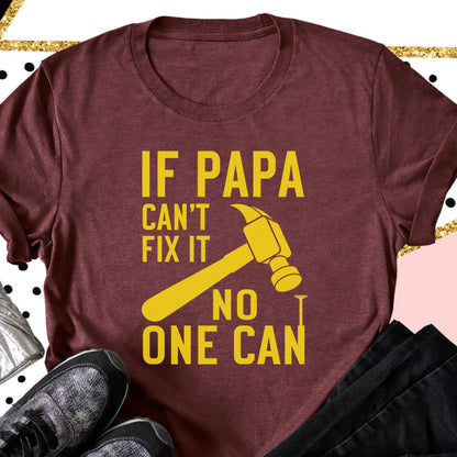 May include: Maroon t-shirt with the text "IF PAPA CAN'T FIX IT NO ONE CAN" in yellow. A yellow hammer graphic is featured. The shirt is a crew neck and has short sleeves.