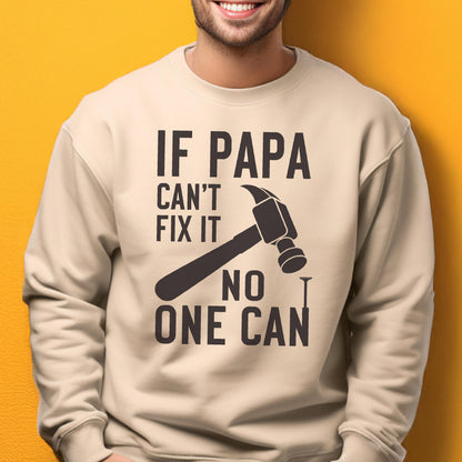 May include: A beige sweatshirt with the text "IF PAPA CAN'T FIX IT NO ONE CAN" in dark brown. A hammer and nail graphic are featured in the center of the design. The sweatshirt is a casual style.